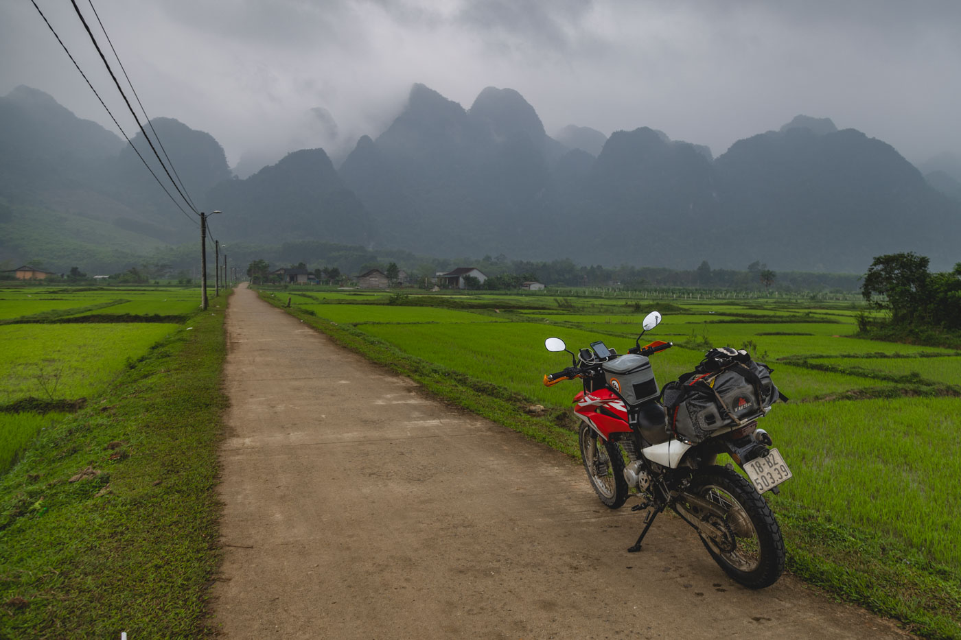 My motorcycle parked on a road in the middle of a rice field with inclement weather coming over the mountains in Vietnam.